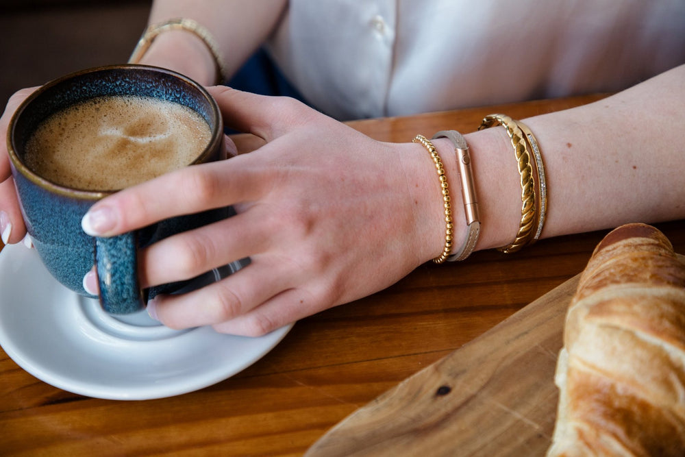 Invi armband gestapeld met andere armbanden bij een kop koffie